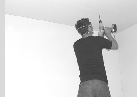 man drilling holes to fit projector lift